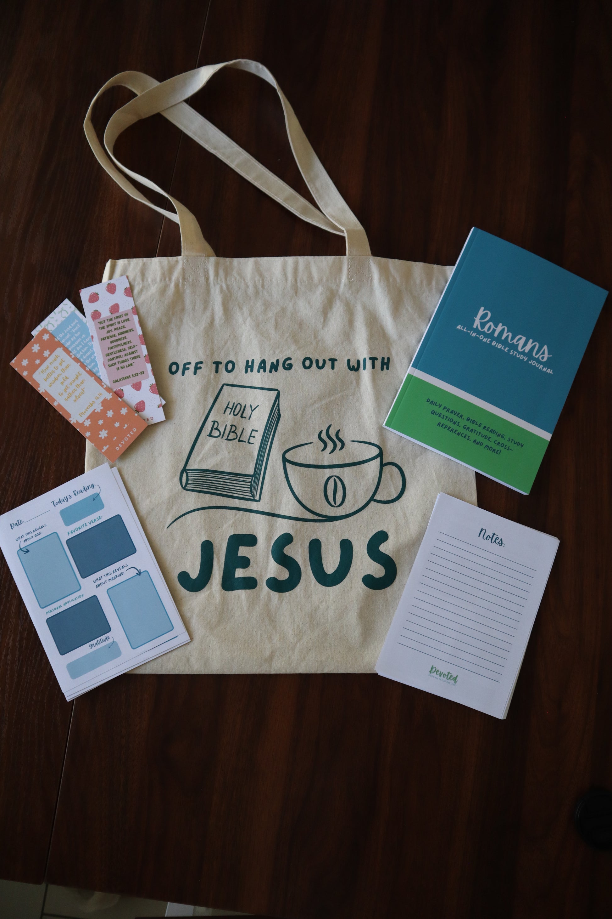 Tote bag with 'Jesus' printed on it, surrounded by cards and a notebook on a wooden surface.
