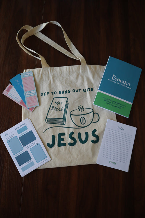 Tote bag with 'Jesus' printed on it, surrounded by cards and a notebook on a wooden surface.