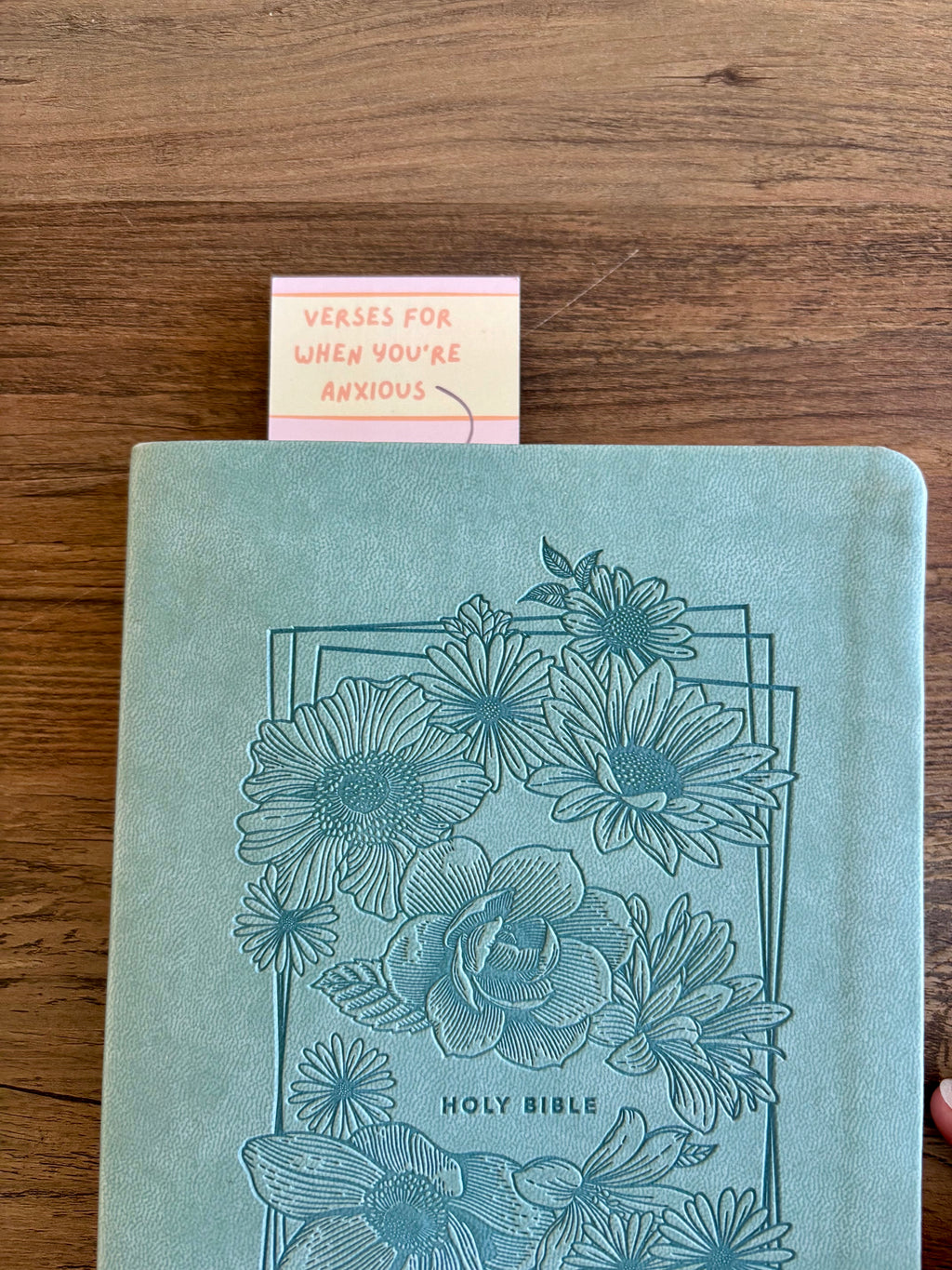 Blue floral embossed Bible on a wooden surface with a small card.