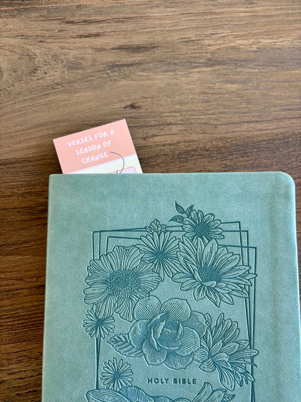 Teal Bible with floral design on a wooden surface