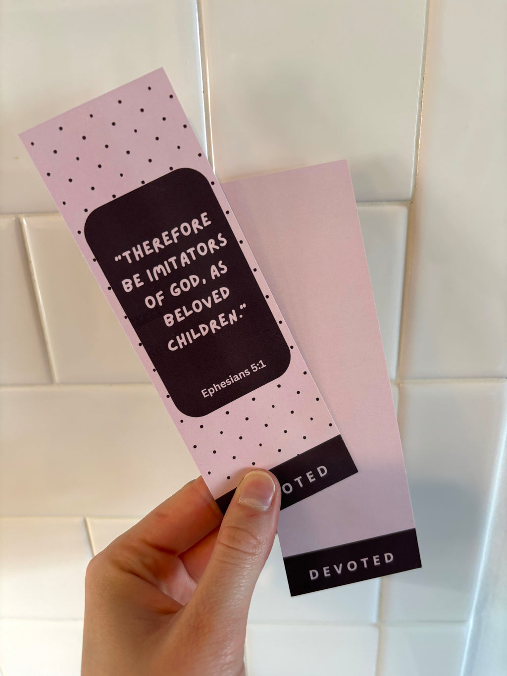 Pink bookmark with text held by a hand against a tiled wall background