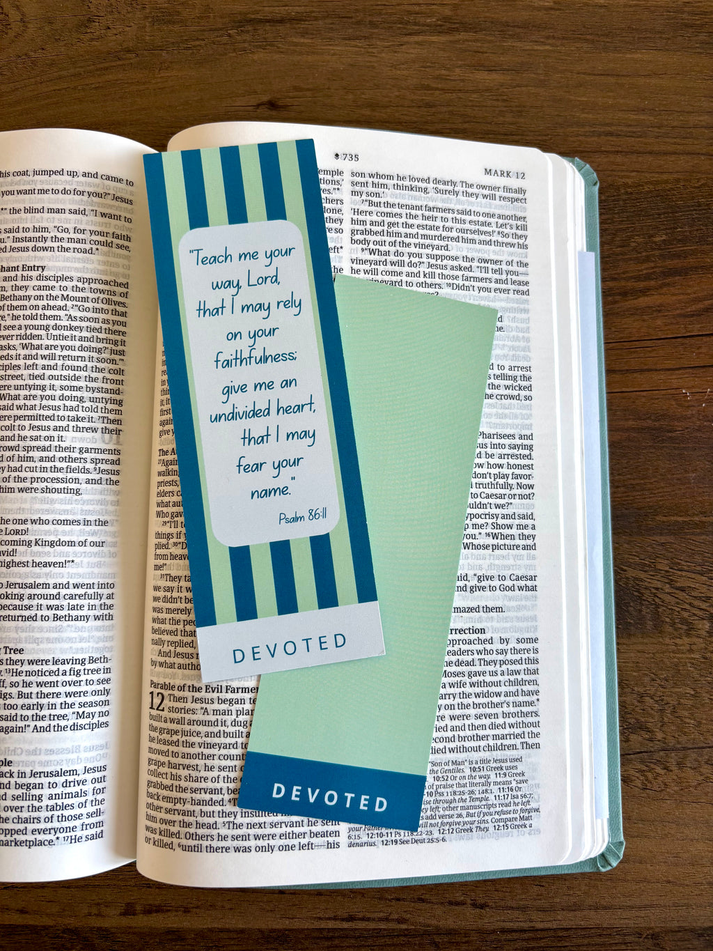 Open book with a bookmark featuring a quote and the word 'Devoted' on a wooden surface.