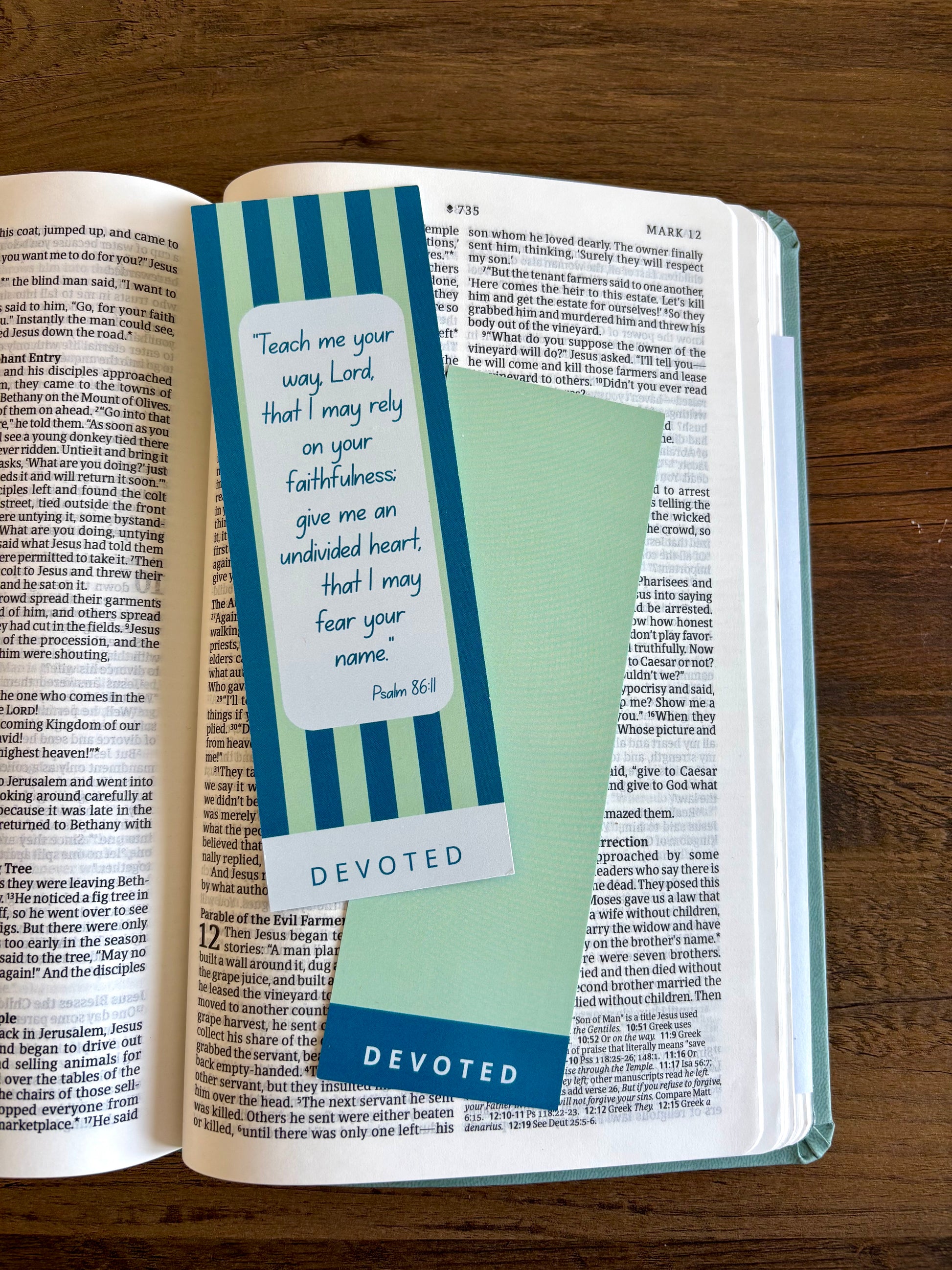 Open book with a bookmark featuring a quote and the word 'Devoted' on a wooden surface.