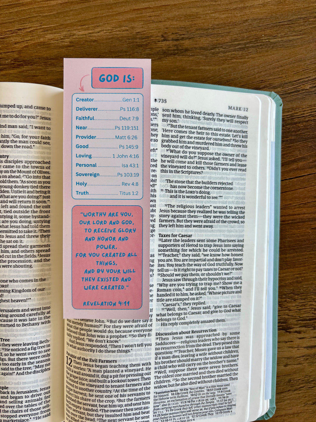 Open book with a pink bookmark titled 'GOD IS' on a wooden surface