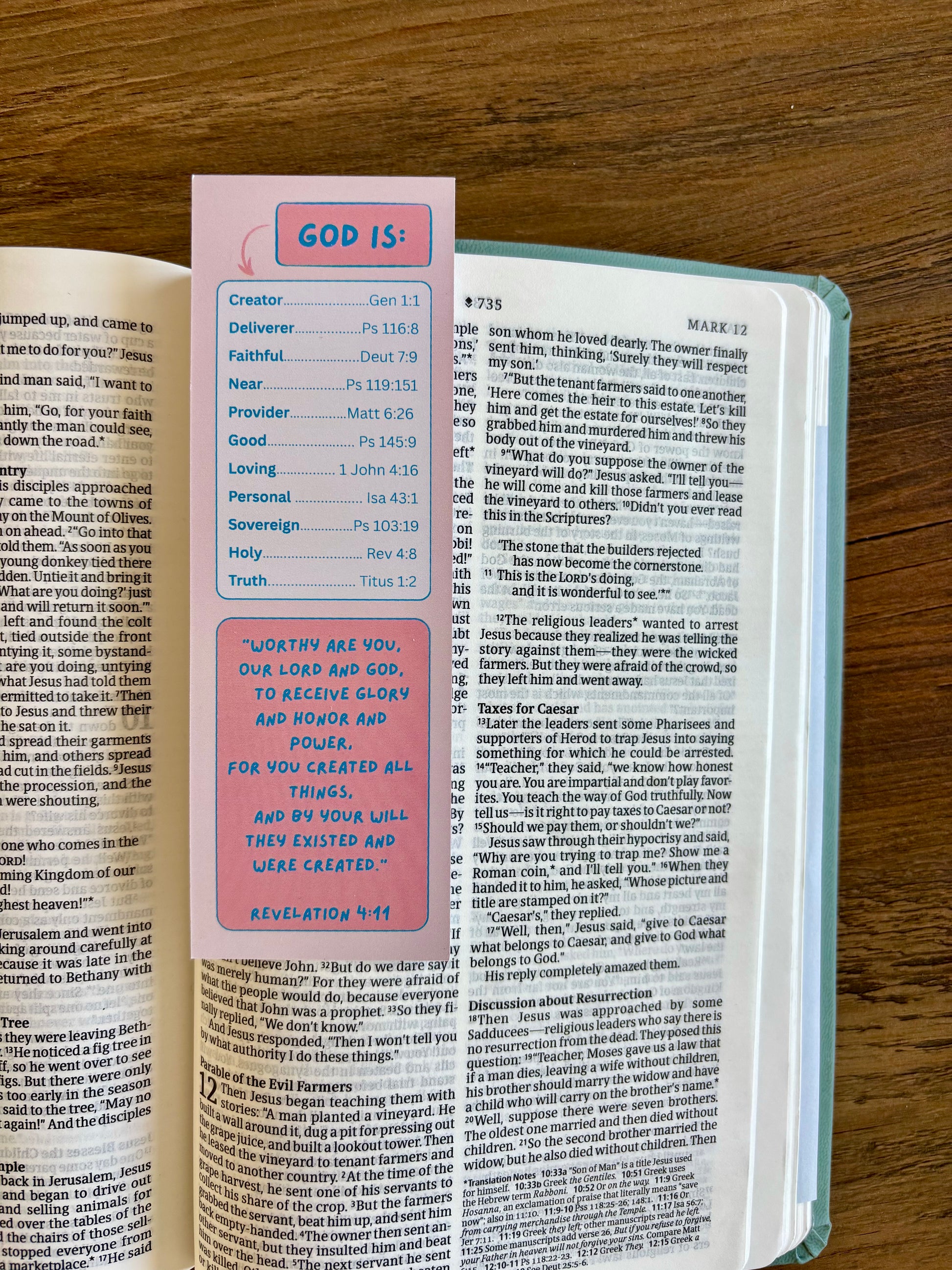 Open book with a pink bookmark titled 'GOD IS' on a wooden surface