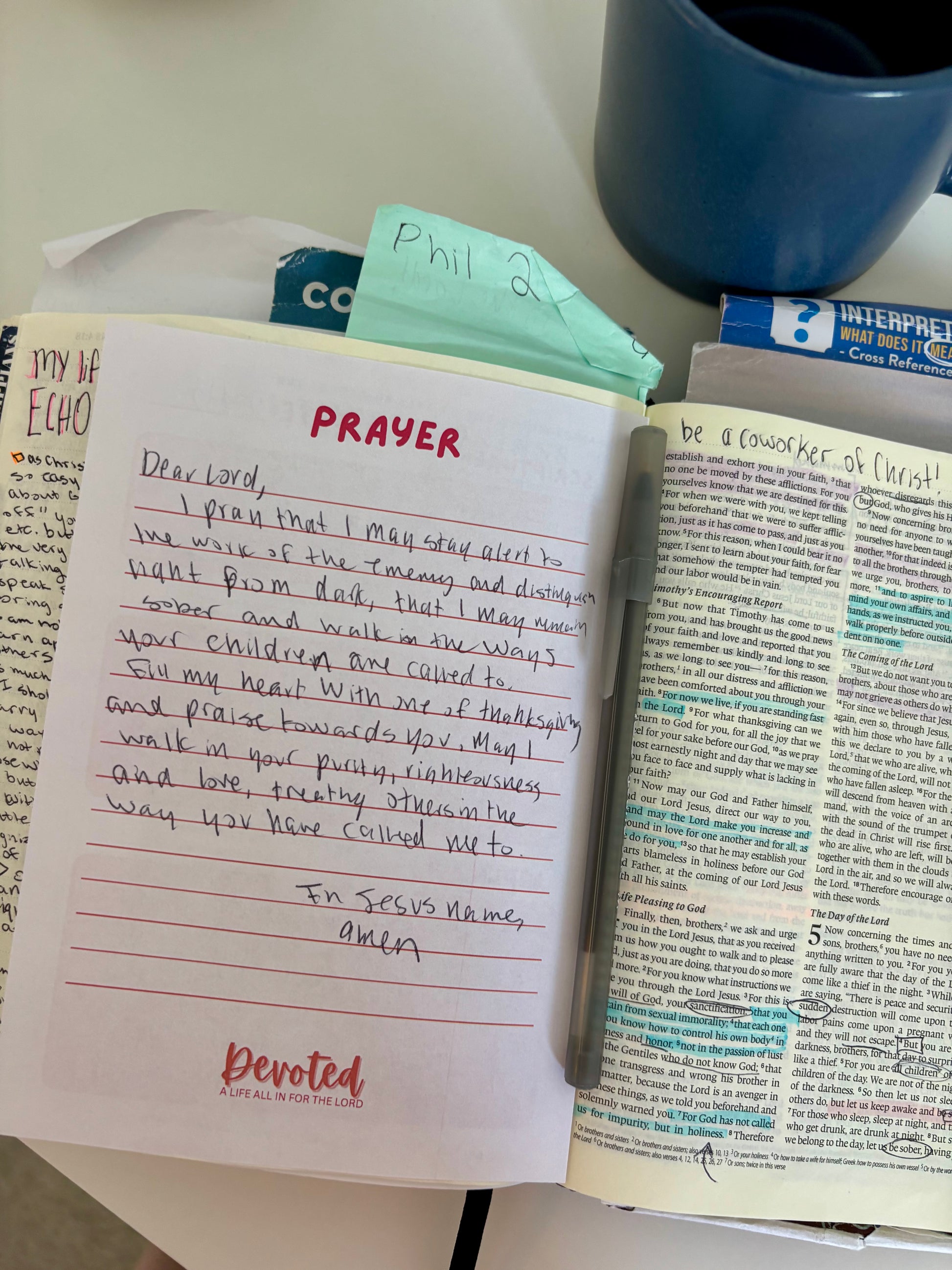 Notebook with prayer written on it, next to a blue mug and open book.