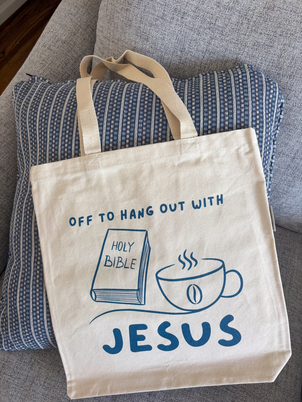 cream canvas tote bag, with navy writting sitting on a coach
