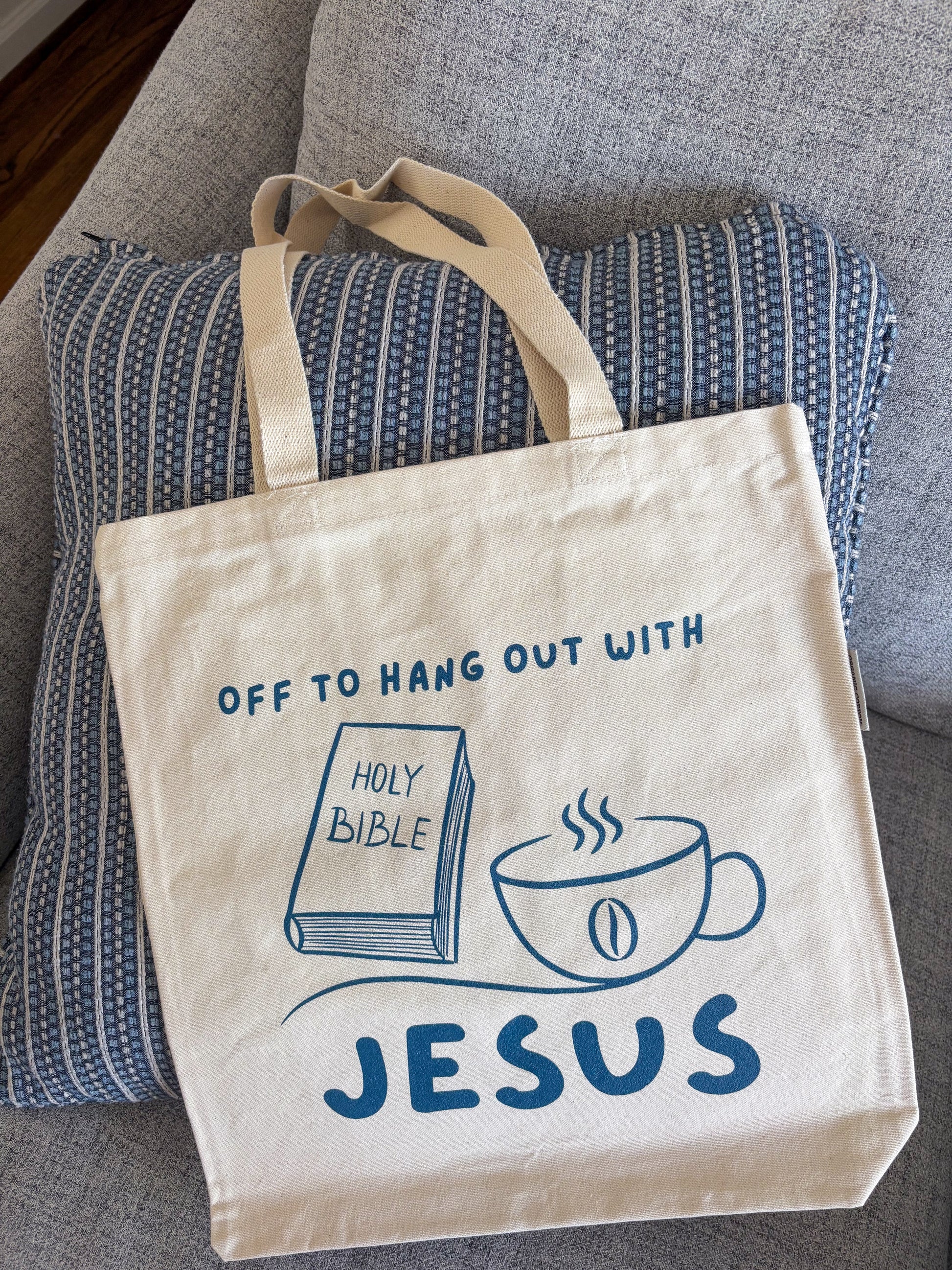 cream canvas tote bag, with navy writting sitting on a coach