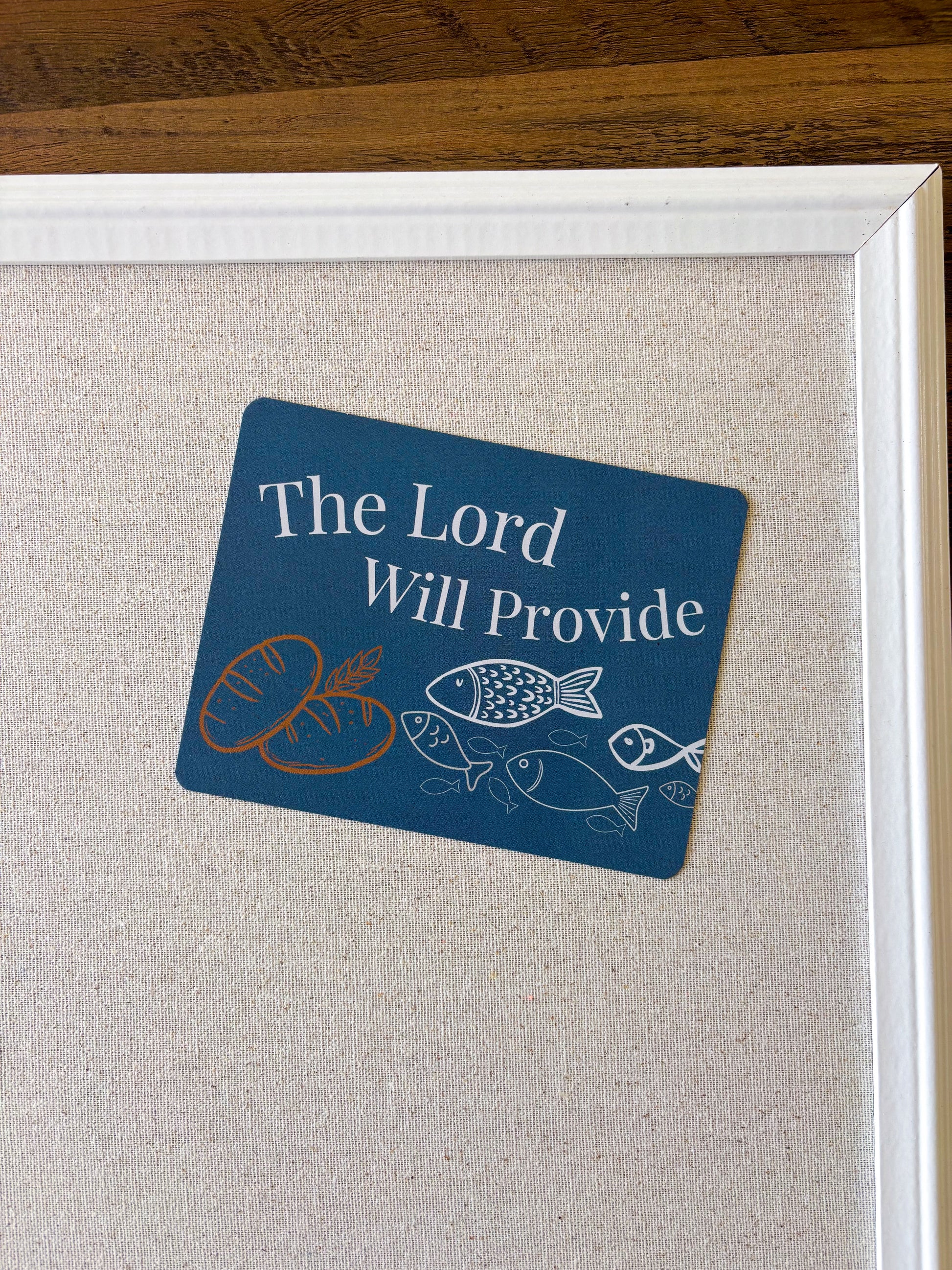 A christian postcard will drawn bread and fish on stating "the Lord will provide" displayed on a cork board.