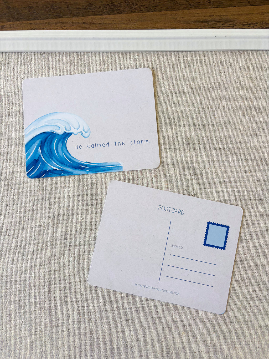 Two postcard-style cards on a textured beige surface. The top card shows a blue ocean wave illustration and the phrase 'He calmed the storm.