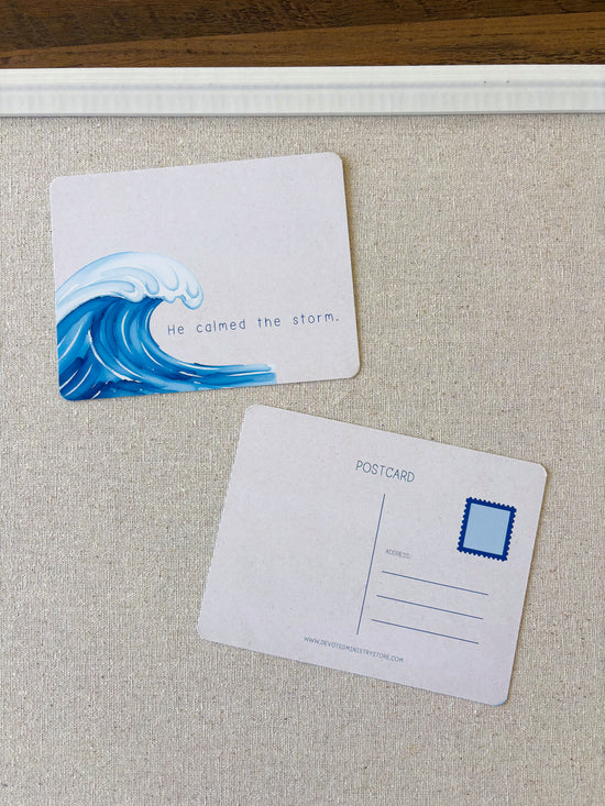 Two postcard-style cards on a textured beige surface. The top card shows a blue ocean wave illustration and the phrase 'He calmed the storm.