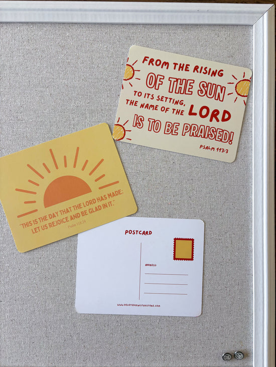 Three decorative postcards featuring Bible verses are arranged on a light gray fabric surface inside a white frame. One postcard is pale yellow with a red sun illustration and a scripture quote from Psalm 103:30.