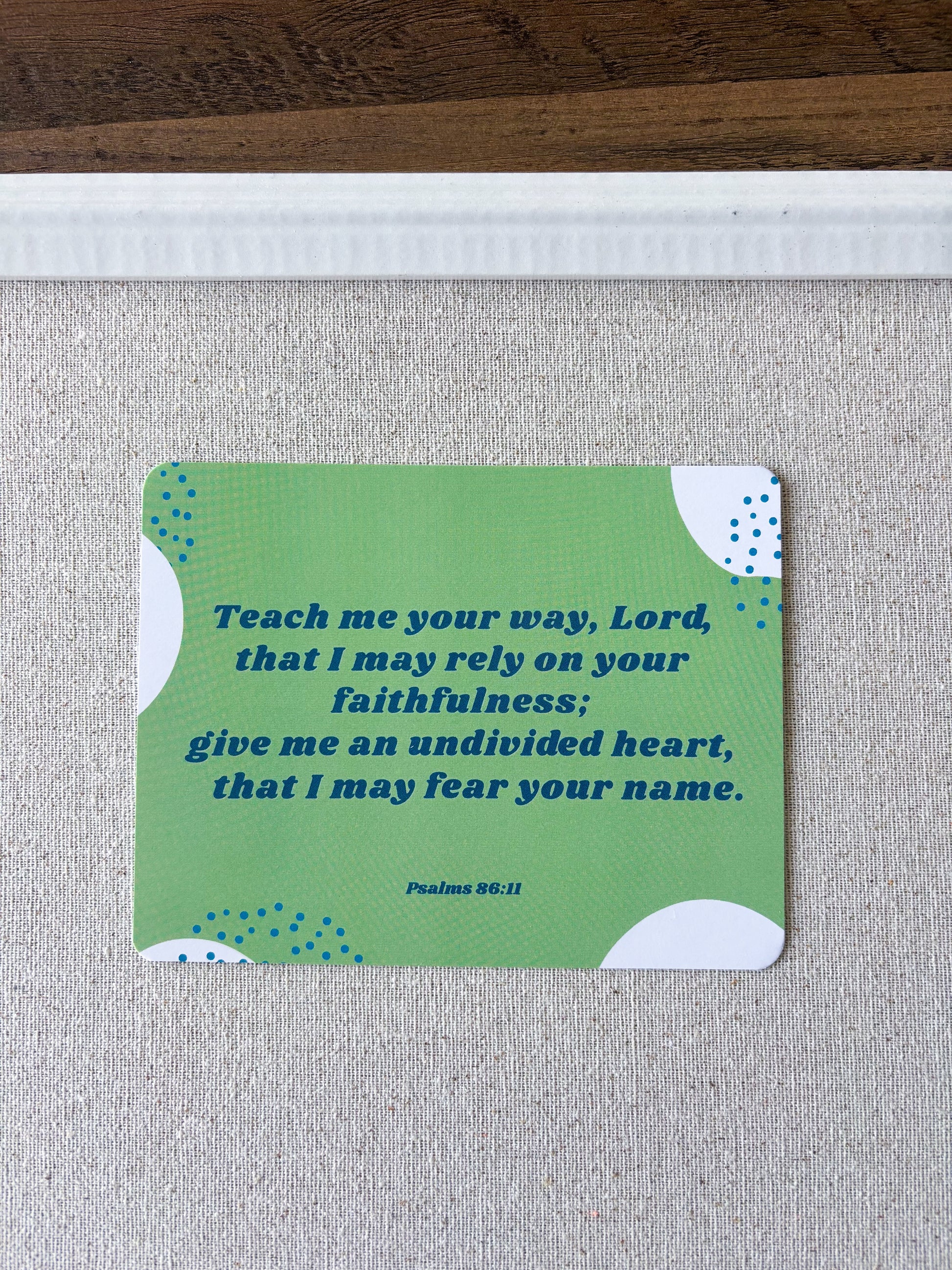 a green postcard with a Bible verse on it, displayed on a cork boar
