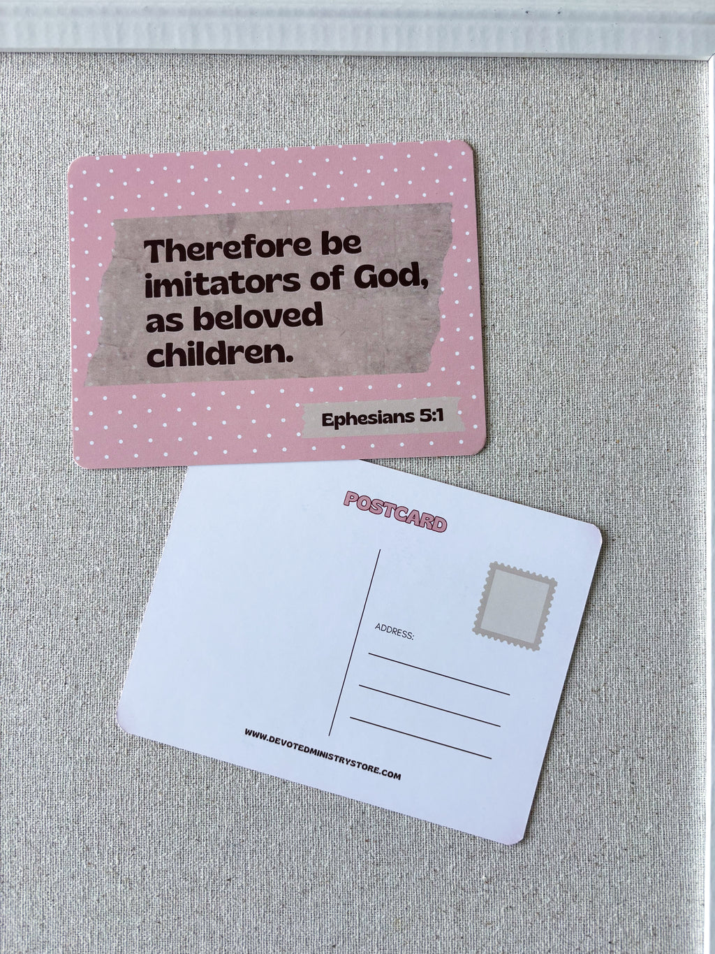 A pink postcard with a Bible verse from Ephesians 5:1 on the front, shown next to the white back side of another postcard on a textured gray surface.