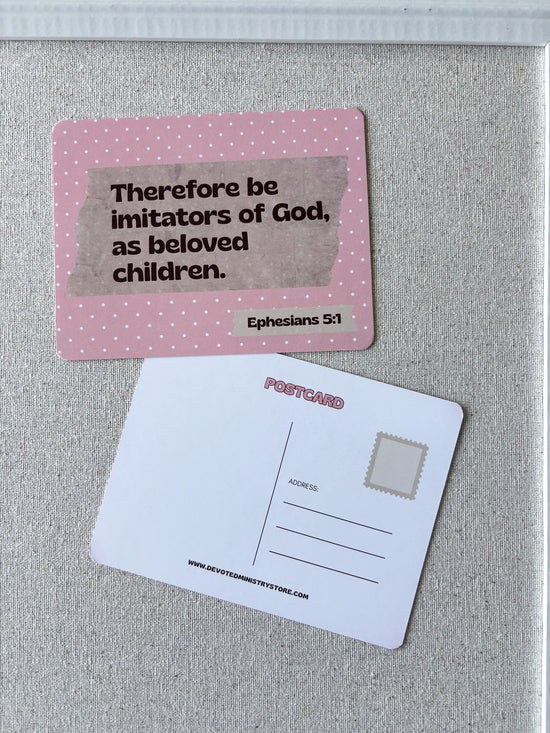 A pink postcard with a Bible verse from Ephesians 5:1 on the front, shown next to the white back side of another postcard on a textured gray surface.