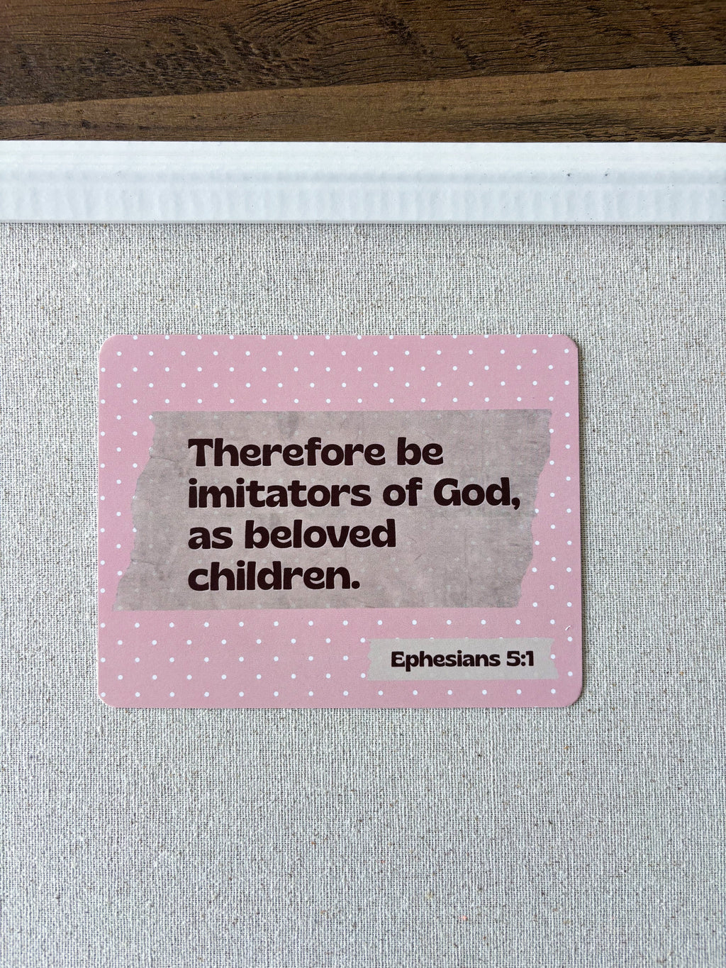 A pink post card with the Bible verse Ephesians 5:1 displayed on a white cork board