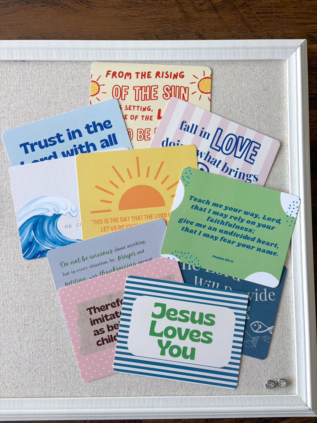 A white-framed display board holding multiple colorful inspirational quote cards arranged on a light fabric background, photographed on a dark wood surface.