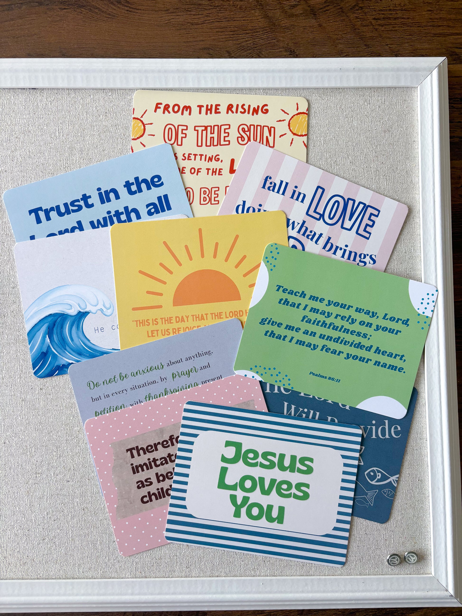 A white-framed display board holding multiple colorful inspirational quote cards arranged on a light fabric background, photographed on a dark wood surface.