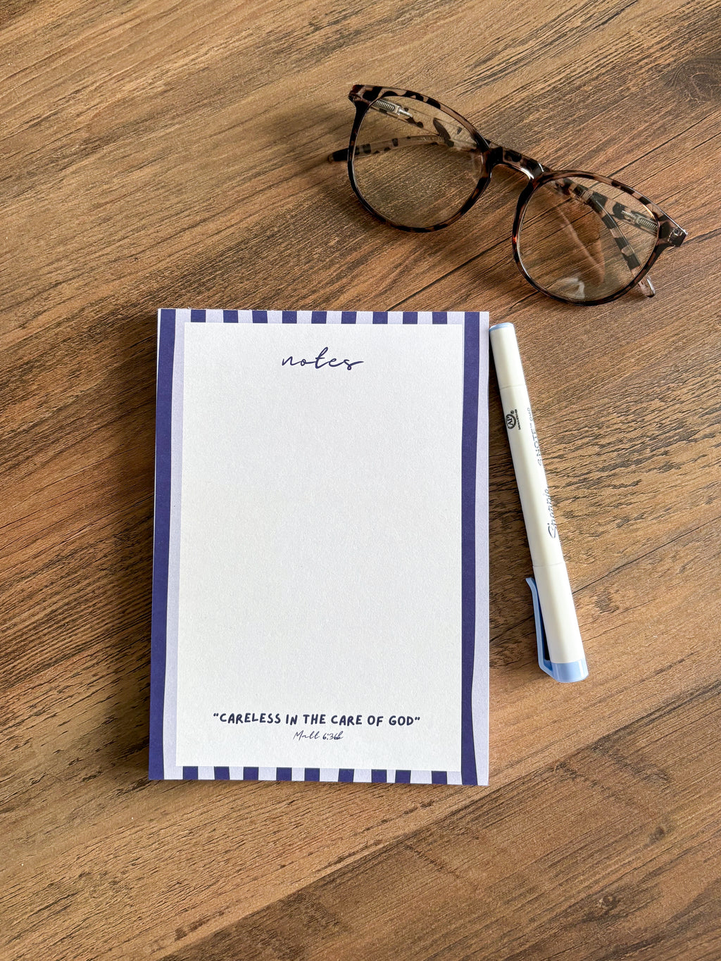 blank notepad with blue stripes on a brown coffee table with a marker and glasses on a table 