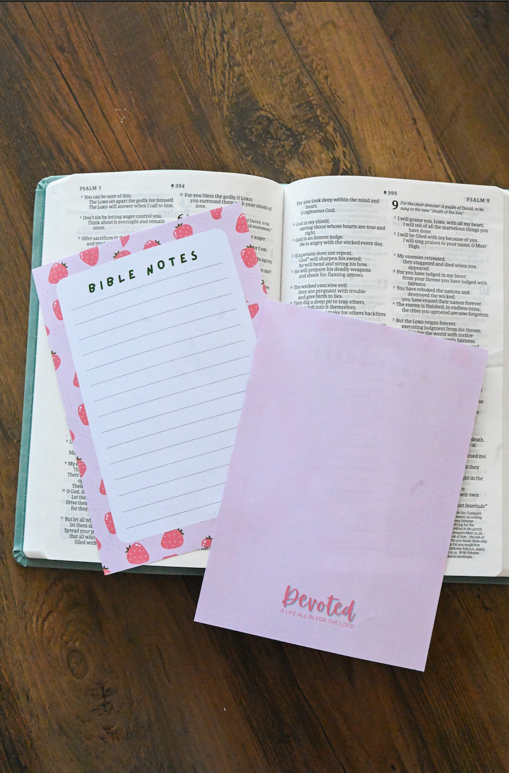 Open Bible with two Christian stationery (journal pages) items on a wooden surface
