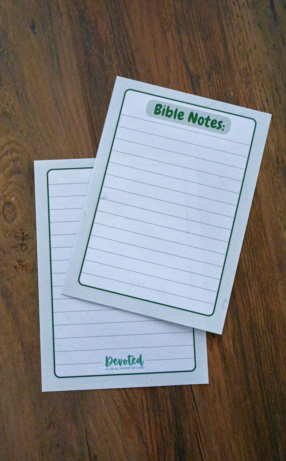 Two sheets of lined paper with 'Bible Notes' and 'Devoted' text on a wooden surface.